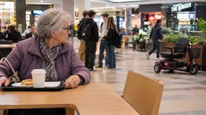 A Senior Lady Keeping an Eye 0on Her Mobility Scooter While Eating in the Food Court